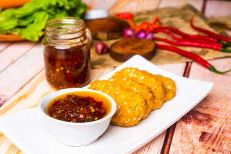 Sambal Bawang, Onion Chili Sauce, with tempeh on white plate, decorated with chilies, onion on wooden tableの写真素材