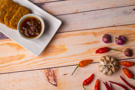 Sambal Bawang, Onion Chili Sauce, with tempeh on white plate, decorated with chilies, onion on wooden tableの写真素材