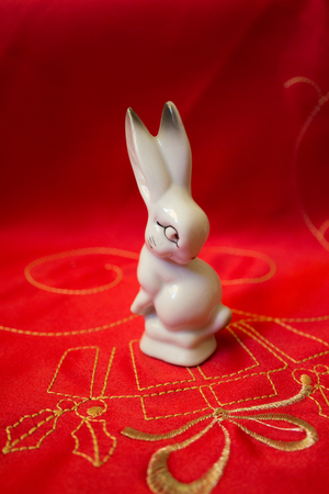 Close up macro shot of a white bunny rabbit made from porcelain on a red textile material with gold stitchingの写真素材