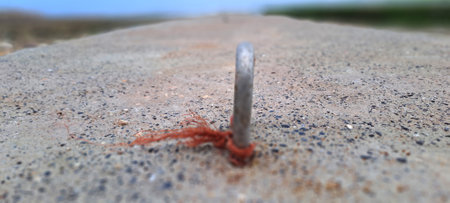 Close-up of a metal ring embedded in a concrete surface, with a piece of red thread attached, possibly used for mooring or securingの写真素材