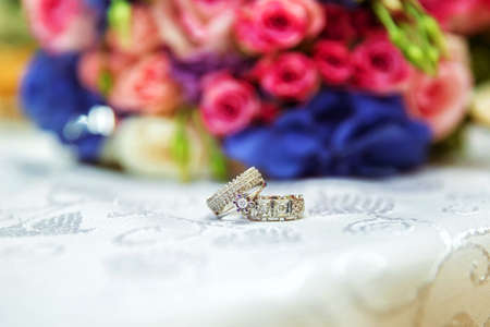 Mens and bridal rings are on the background of a multi-colored wedding bouquet