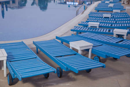 Empty sunbeds by the beautiful resort pool . Lounge sunbeds near swimming pool .Sun loungers by the...