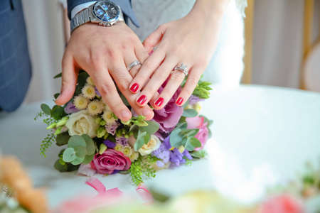 Bride and groom with Engagement gold rings put their hands on the table, and next to them lies a wedding bouquet .Engagement flowers .The girl and the boy put their hands on colorfull roses.の写真素材
