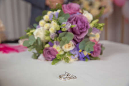 wedding rings and beautiful bouquet as bridal accessories . Beautiful toned picture with Engagement rings lie on a wooden surface against the background of a bouquet of flowersの写真素材