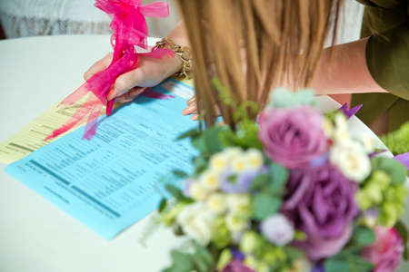 the bride in a wedding dress signs in the contract close up . Hands of Caucasian wedding people signing the document on wed ceremony, close up view . The newlyweds put their signature on the marriageの写真素材