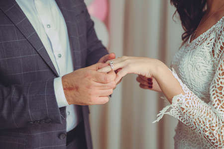 Puts a ring on the bride's hand . Groom puts wedding ring on bride's hand in church .Man puts a wedding ring on a bride's hand, close-up photoの写真素材