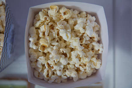 A wide classic box of theater popcorn isolated on white . Popcorn spilled from a striped box . Three...