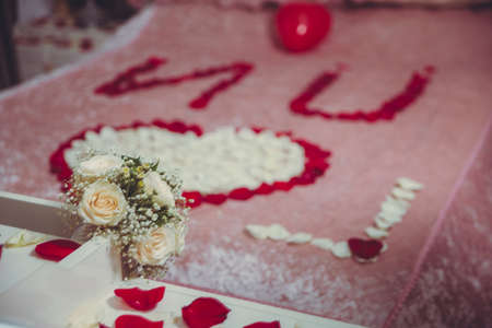 White flower bouquet for the wedding.. A heart made of petals on the beds. Red petals. Close up of white flowers in the bed . White wedding dress bouquet lying on the bed.の写真素材
