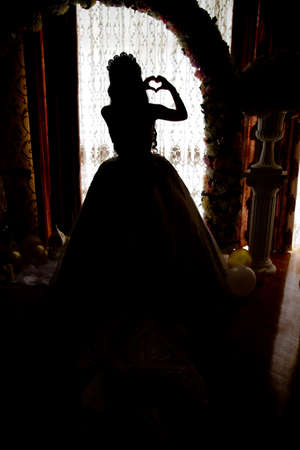 The back side of a white wedding dholds a heart in his handress. The bride looks out of the huge window in the bridal suite revealing the backside of the wedding dressの写真素材