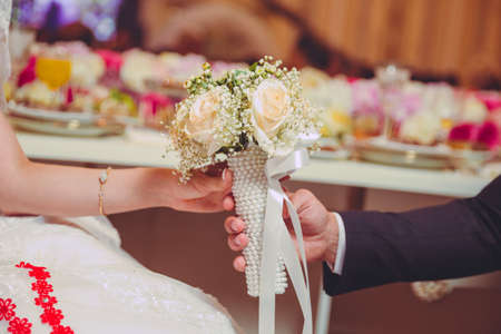 Hands folded behind their back, hold a beautiful white little wedding bouquet of roses . They held the white flower bouquet in their handsの写真素材