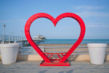 Heart decor in the sea . Red heart decoration a place to sit . Red iron holiday lovely decorative love bench in the seaの写真素材