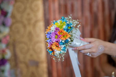 coloured macro photo of a detailed bouquet with colorfull roses, white small flowers and a fake diamond in the centre of the rose . He holds a wedding flower in his handの写真素材