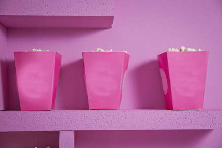 A wide classic box of theater popcorn isolated on pink . Popcorn spilled from a striped box . Three vintage-style boxes of popcorn in a carnival themed still life with arcade game pink ticketsの写真素材