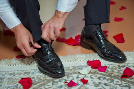 Man wearing a suit putting his brown shoes on. Hands and shoe close-up. Closeup view of male hands lacing beautiful elegant shoes. wedding day. groom tie his shoeの写真素材