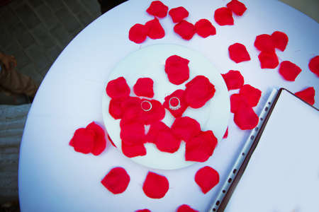 Rings and red petals inside the white plate . A table designed for engagement. Table setting in honor of Valentine's Day close-upの写真素材
