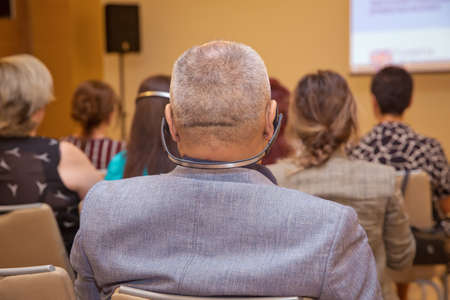 bald security guard with the headset to control people . heated debate at a conference discussion . Unrecognizable man using headphones for translation during video conference .の写真素材