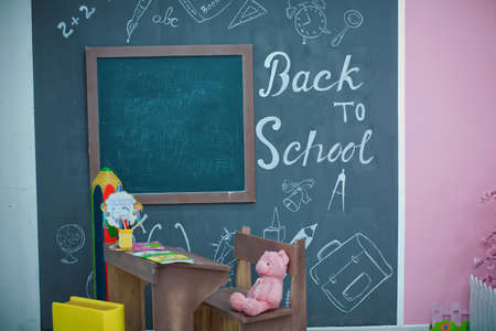Back to school. Happy smiling pupil drawing at the desk. class room with blackboard on background. Alarm clock, pencils, books. first day of fall.Back to school concepty with writing on blackboardの写真素材