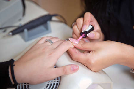 The master does a manicure in the salon, close-up. He paints his nails with white lacquer.Beautician painting client's nails with transparent lacquer during manicure process in a beauty salon. Conceptの写真素材