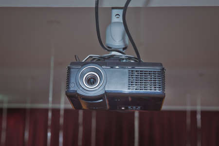 Black Projector hang on white ceiling in big meeting room or university. A white overhead projector on ceiling indoors. Modern video projector on ceiling in roomの写真素材