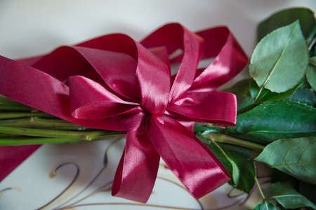 Red rose with bow . atlas ribbon bow on bouquet of flowers . Red ribbon tied into bow at bouquet of flowersの写真素材