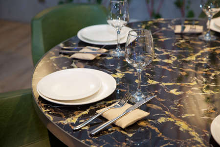 Set of cutlery knife, spoon, fork, plate, wine glass. Black marble table . Green chair.の写真素材