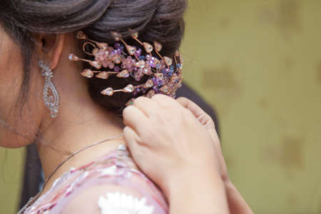 He wears a necklace around his neck. Groom wearing a necklace to the bride. mother of bride helping...