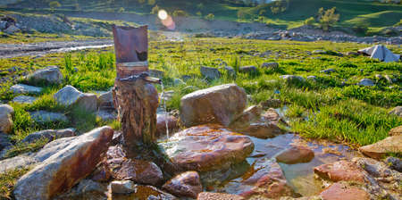 Water flowing from pipe against blurred mountain background. iron pipe flowing clean drinking water . spring water from the ground Colorfull red stone .の写真素材