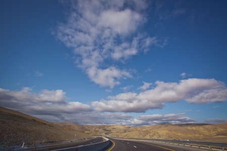 Open road with blue clouds . Asphalt road and bright blue sky with fluffy clouds . Empty desert asphalt road from low angle with mountains and clouds on background. road, red desert landscapeの写真素材