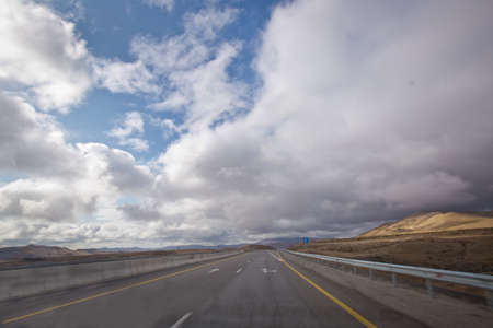 Open road with blue clouds . Asphalt road and bright blue sky with fluffy clouds . Empty desert asphalt road from low angle with mountains and clouds on background. road, red desert landscapeの写真素材