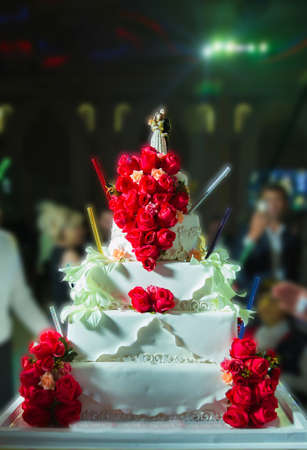 Wedding cake with red roses flowers . Colorful cakes for the occasion. Close-up . Beautiful Wedding Cake with Rose Flowers Decoration . Rose covered wedding cake at reception table . 5-storey cakeの写真素材