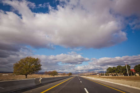 Open road with blue clouds . Asphalt road and bright blue sky with fluffy clouds . Empty desert...