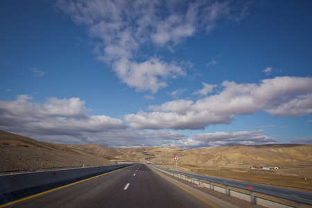 Open road with blue clouds . Asphalt road and bright blue sky with fluffy clouds . Empty desert asphalt road from low angle with mountains and clouds on background. road, red desert landscapeの写真素材