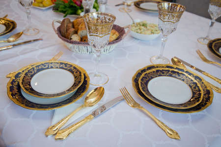 Beautifully decorated table with gold plates, linen napkin , spoon, fork . Empty plate , gold set on wooden white table .の写真素材
