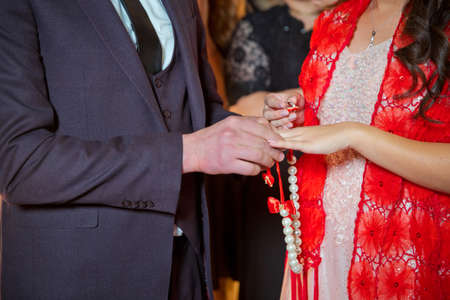 room Dresses the Ring for the Bride, close-up. Newlyweds exchange rings, groom puts the ring on the bride's hand in marriage registry office . The brides is wearing a ring on the bride's hand .の写真素材