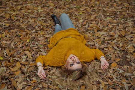 beautiful girl in the park between the leaves in front of the tree in autumn. photo session in the fall of a blond beautiful girl in the park between the leaves . Baku Azerbaijan 21.12.2019 .のeditorial素材