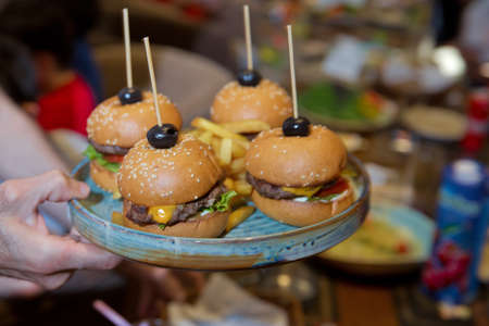 Waiter carrying a tray of appetizers. Outdoor party with finger food, burgers, sliders. man hold...