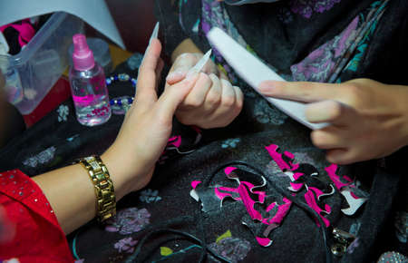 Each of the nails is filed before the artwork is painted onto the nail. Rough up the top of the nail for better adhesion. Manicure in beauty salon. Selective focus on nail polish removing pen.の写真素材
