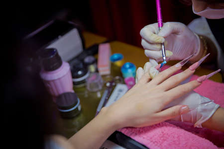 Manicure hands salon . Woman in a nail salon receiving a manicure by a beautician . Manicure process in beautiful salon . Closeup of Woman applying nail varnish to finger nailsの写真素材