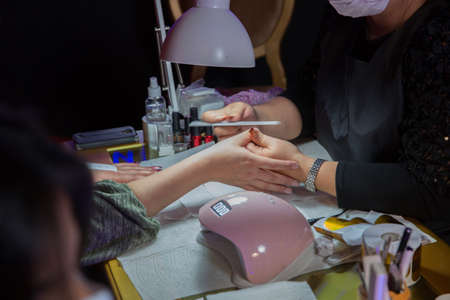 Manicure hands salon . Woman in a nail salon receiving a manicure by a beautician . Manicure process in beautiful salon . Closeup of Woman applying nail varnish to finger nailsの写真素材