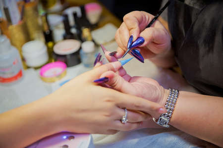 Manicure hands salon . Woman in a nail salon receiving a manicure by a beautician . Manicure process in beautiful salon . Closeup of Woman applying nail varnish to finger nailsの写真素材
