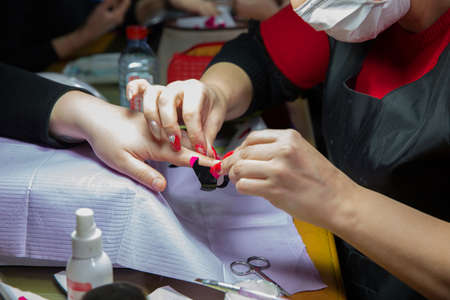 Manicure hands salon . Woman in a nail salon receiving a manicure by a beautician . Manicure process in beautiful salon . Closeup of Woman applying nail varnish to finger nailsの写真素材
