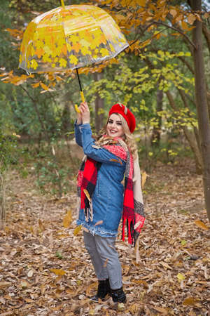 Baku Azerbaijan 21.12.2019 . photo session park between the leaves in front of the tree in autumn. The girl in the red hat is holding an umbrella, smiling and looking at the cameraのeditorial素材