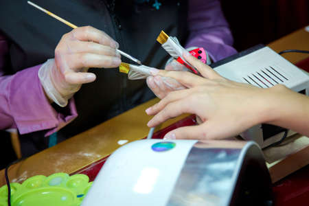 Manicure hands salon . Woman in a nail salon receiving a manicure by a beautician . Manicure process in beautiful salon . Closeup of Woman applying nail varnish to finger nailsの写真素材