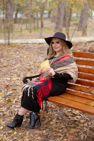 Baku Azerbaijan 21.12.2019 . photo session beautiful girl in the park between the leaves in front of the tree in autumn. girl is sitting on a bench in the park and reading a bookのeditorial素材