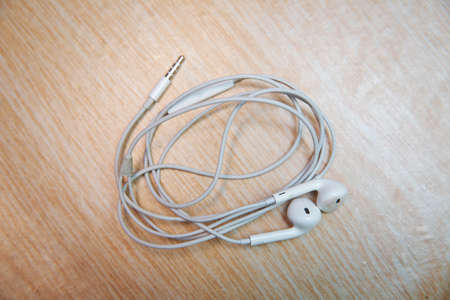 Earbud or earphone top view on wooden background . White earphones from the phone