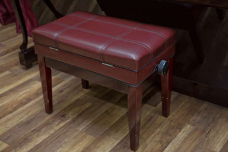 Big brown wooden piano and red bench close up in room . Old wooden piano keys on wooden musical instrument in front view . modern red leather piano benchの写真素材