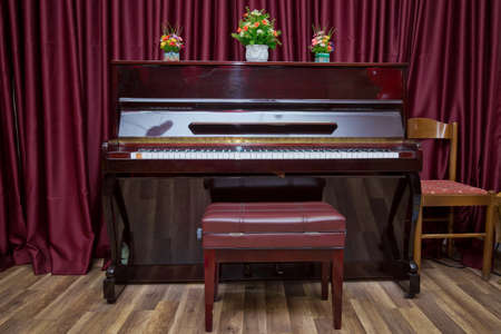 Big brown wooden piano and red bench close up in room . Old wooden piano keys on wooden musical instrument in front view . modern red piano benchの写真素材