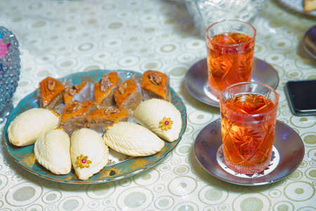 Baklava and Shekerbura blue plate . Glass of Azerbaijan tea isolated on white . Cup of tea isolated on white tablecloth . Shekerbura with nuts and honey.の写真素材
