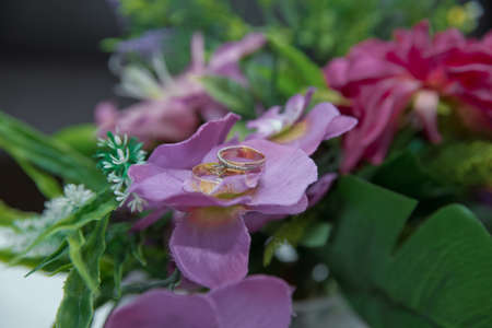 A pair of gold wedding rings . Rings on the petals of artificial pink flowers .の写真素材