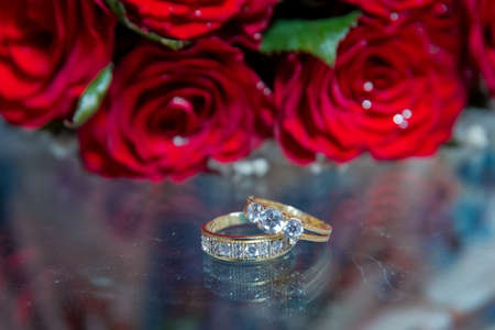 Glass table . Wedding rings next to a red flower bouquet selective focuse . Bride and groom with Engagement gold rings put on the table, and next to them lies a wedding bouquet .の写真素材